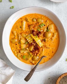 a white bowl filled with stew and corn on the cob next to a spoon