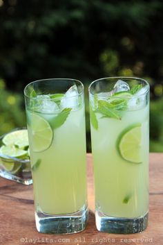 two glasses filled with limeade on top of a wooden table