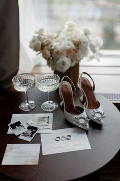 a table topped with two wine glasses and some shoes next to a vase filled with flowers