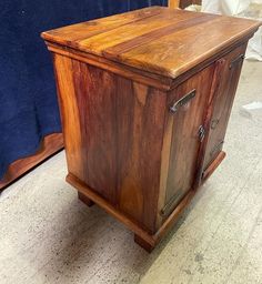 a wooden cabinet sitting on top of a floor next to a blue sheet covered wall