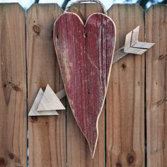 a wooden heart hanging on the side of a fence with an arrow and two triangles