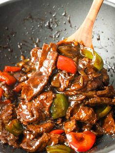 beef and peppers being cooked in a wok with a wooden spoon on the side