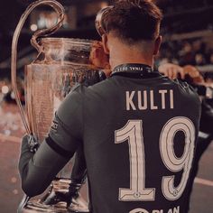 a man holding a soccer trophy in his hands and looking at the other team's shirts