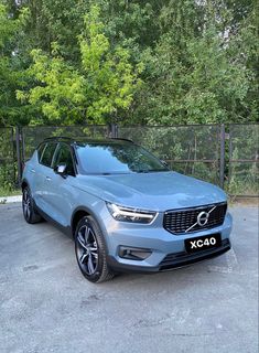 a blue volvo car parked in a parking lot next to some trees and fenced in area