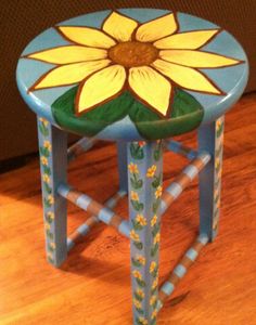 a painted stool with a sunflower on the top and bottom, sitting on a wooden floor