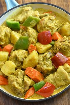 a pan filled with chicken and vegetables on top of a wooden table