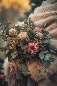 a woman holding a bouquet of flowers and greenery in her hands, wearing a sweater