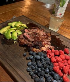 a wooden cutting board topped with meat and fruit next to a glass of water on top of a table