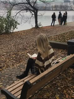 a woman sitting on top of a wooden bench next to a tree filled with leaves