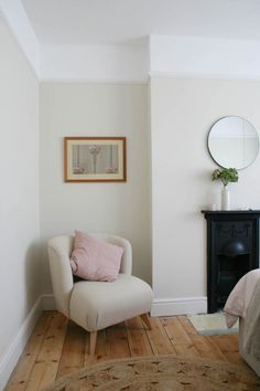 a white chair sitting on top of a hard wood floor next to a mirror and fireplace