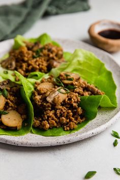 two lettuce wraps filled with meat and vegetables on a white plate next to a wooden spoon