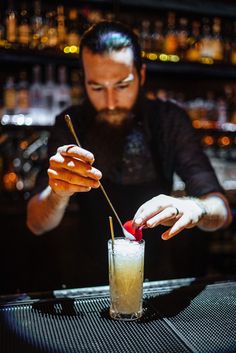 the bartender is making a drink at the bar with his hand on the glass and holding a straw in front of him