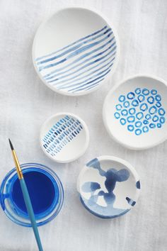 three bowls with blue paint and one has a brush next to it on a white tablecloth