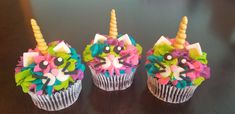 three cupcakes decorated with colorful icing and unicorn decorations on top of a table