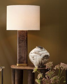 a lamp on a table next to a vase with flowers in it and a wooden stand