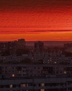 the sun is setting over a city with buildings in the foreground and red sky