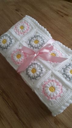 a white crocheted blanket with pink ribbon and flowers on the front, sitting on a wooden surface