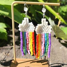 a pair of earrings with beads hanging from it's sides on a wooden stand