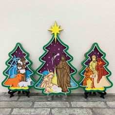 three wooden christmas trees with nativity scenes in them on a brick floor next to a white wall