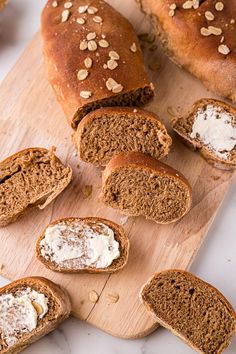 several loaves of bread sitting on a cutting board with butter and nuts around them