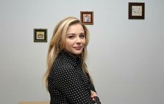 a woman standing in front of a wall with pictures on it