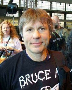 a man with long hair standing in front of a group of people