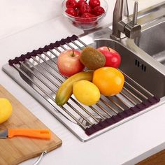 fruits and vegetables are sitting on a rack in the kitchen sink next to a cutting board