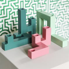 three lego blocks sitting on top of a white table next to a wall with green and pink designs