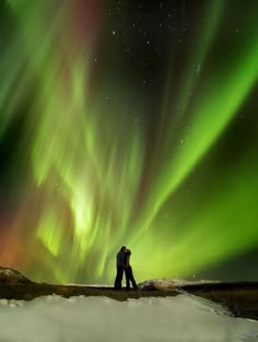 two people are standing in the snow under an aurora borel sky with green and red lights