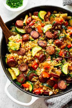 a skillet filled with sausage, zucchini and other vegetables on top of a table