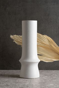 a white vase sitting on top of a table next to a large stalk of wheat