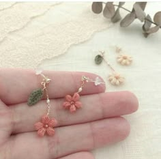 the tiny flower earrings are on someone's hand, and they have leaves attached to them