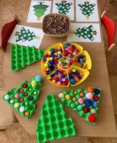 three trays with different shapes and balls in them on a table next to a bowl of pom - poms