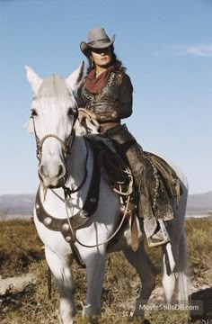 a woman riding on the back of a white horse in an open field with mountains in the background