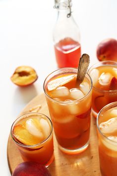 four glasses filled with ice and fruit on a wooden tray next to some sliced peaches