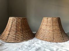 two woven lampshades sitting on top of a white sheet covered bed next to each other