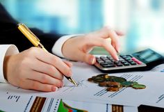 a person with a pen and calculator sitting at a desk next to stacks of money