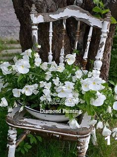 an old chair with flowers in it is sitting on the grass next to a tree