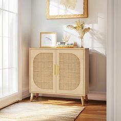 a white cabinet with wicker doors and gold handles in front of a painting on the wall