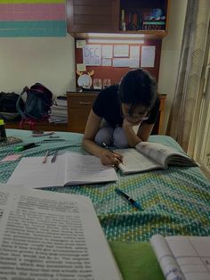 a woman sitting on top of a bed reading a book and holding a pen in her hand