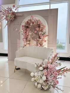 a white couch sitting in front of a window next to a bunch of pink and white flowers