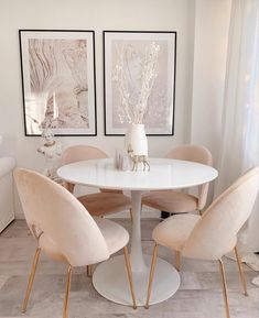 a white table with four chairs around it and two pictures on the wall behind it