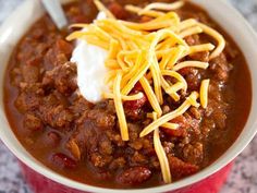 chili with cheese and sour cream in a red bowl on a counter top, ready to be eaten