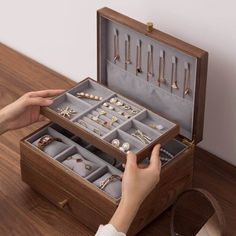 a woman is holding an open wooden box with jewelry in it on top of a table