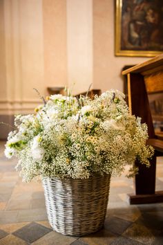 a basket filled with lots of white flowers sitting on top of a floor next to a wooden bench