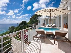 an outdoor deck with chairs and umbrella overlooking the ocean