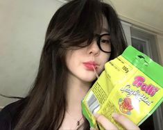 a woman with long hair and glasses holding a bag of noodles in her hand while looking at the camera