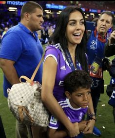 a woman holding a young boy in her arms at a soccer game with other people