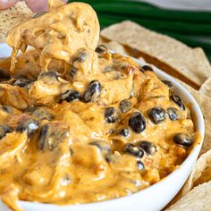 a bowl filled with black olives and cheese dip surrounded by tortilla chips