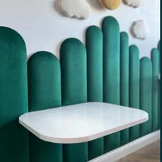 a white table sitting next to a green wall with clouds on the wall behind it